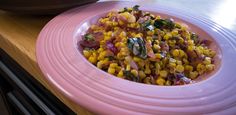 a pink bowl filled with corn on top of a wooden table