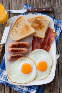 a plate with eggs, sausages and toast on it next to a glass of orange juice