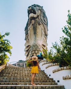 a woman in a yellow dress and straw hat walking up some steps to a large statue