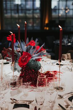 a centerpiece with red flowers and candles on a white table cloth in a restaurant