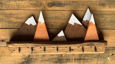 three wooden mountains are mounted on a wood board with metal pegs to hold them