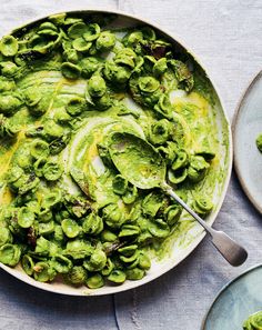 a bowl filled with green vegetables and sauce on top of a table next to plates