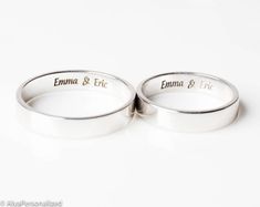 two wedding rings with names engraved on the sides, set against a plain white background