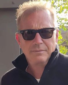 a man wearing sunglasses and a black jacket is looking at the camera while standing outside