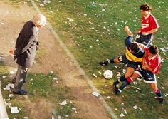 an old man kicking a soccer ball on the field with other men around him and confetti all over the ground