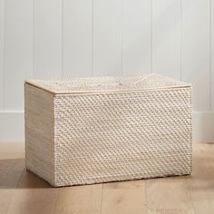 an empty wicker box sitting on the floor in front of a white wall and wooden floors