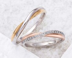 two wedding bands with diamonds on them sitting on a marble surface in front of a white background