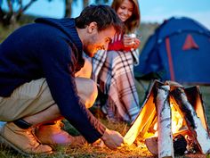 a man and woman sitting next to a campfire with a tent in the background