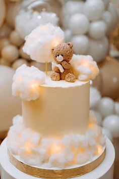 a teddy bear sitting on top of a white cake with clouds and lights around it