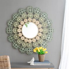 a mirror on the wall above a table with a vase and flowers in front of it