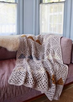 a crocheted blanket on a couch in front of two windows with blue walls