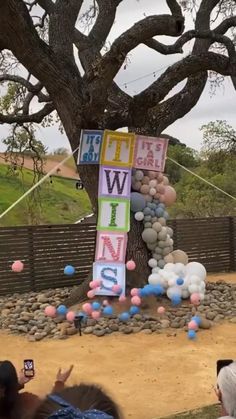 a group of people standing in front of a tree with balloons and letters on it