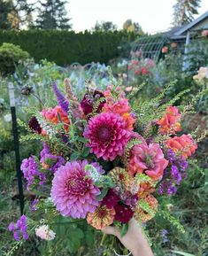 a person holding a bouquet of flowers in their hand with many other flowers around them