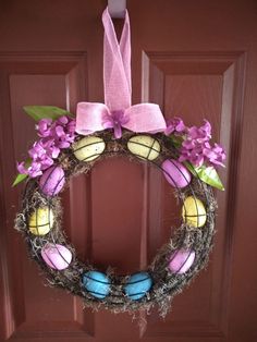 a wreath with purple flowers and eggs hanging from the front door, decorated with pink ribbon