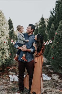 a man holding a child in his arms while standing next to two women and trees