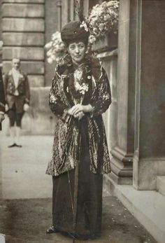 an old black and white photo of a woman dressed in costume standing on the sidewalk