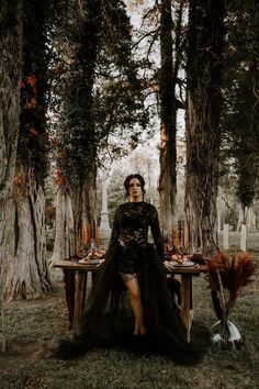 a woman sitting at a table in the middle of a forest with candles on it