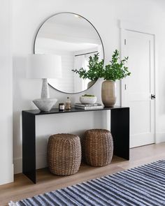 a table with two stools and a round mirror on the wall above it in a white room