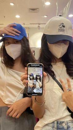 two women wearing face masks and holding up their cell phones