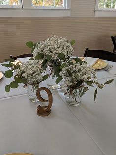 two vases filled with flowers on top of a white table cloth covered round table