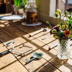 a vase filled with flowers sitting on top of a wooden table next to utensils