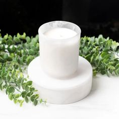 a white candle sitting on top of a table surrounded by greenery