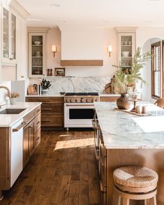 a kitchen with wooden flooring and white walls, an oven, sink, counter tops, and stools