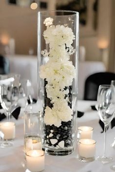 a tall vase filled with white flowers on top of a table next to glasses and candles