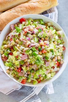 a white bowl filled with salad next to a baguette roll on top of a table