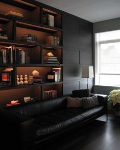 a living room filled with black furniture and bookshelves next to a large window