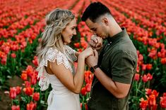 a man and woman standing next to each other in front of a field of flowers