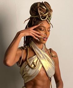 a woman with dreadlocks on her head wearing a gold top and silver skirt