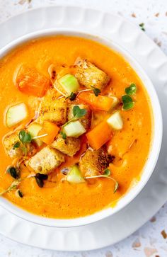 a bowl of carrot soup with croutons, bread and garnishes