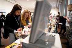 two women looking at items on display in a room with other people standing around it