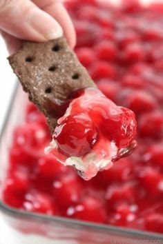 a hand holding a cracker over a bowl of cherries