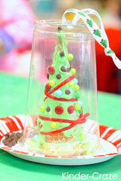 a small green christmas tree in a glass container on a plate with candy and ribbon