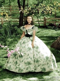 a woman in a green and white dress sitting on the ground next to some flowers