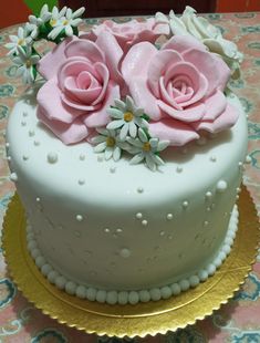 there is a white cake with pink roses and daisies on the top, sitting on a gold plate