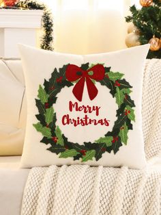 a christmas wreath pillow sitting on top of a couch next to a white sofa cushion