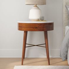 a small table with a lamp on it next to a bed in a white room