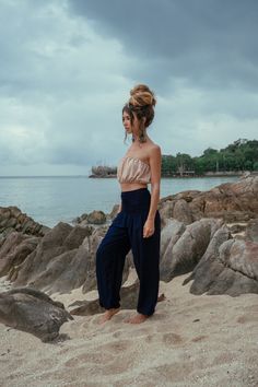 a woman standing on top of a sandy beach next to the ocean with her hands in her pockets