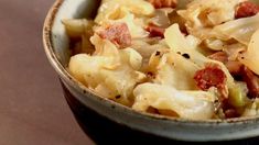 a close up of a bowl of food with noodles and meats in it on a table