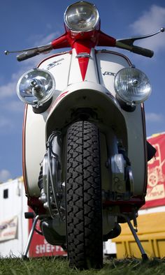 the front end of a white and red scooter parked on top of grass