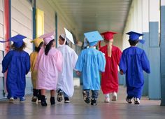 several children in graduation gowns walking down the hallway with one child wearing a cap and gown