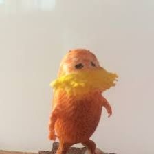 a toy bird with yellow feathers on it's back legs and feet sitting on a table