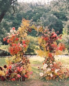 an arch made out of flowers and leaves in the middle of a field with trees behind it