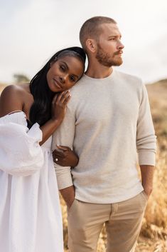 a man and woman are standing in the grass, one is holding his arm around the other's shoulder