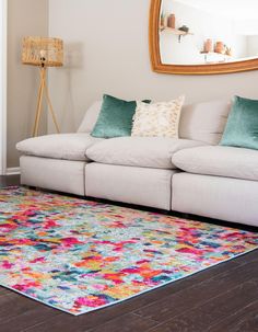 a living room with a white couch and colorful rug on the wooden floor next to a mirror