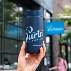 a person holding up a coffee cup in front of a building