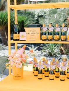 bottles of champagne are lined up on a yellow shelf in front of flowers and plants